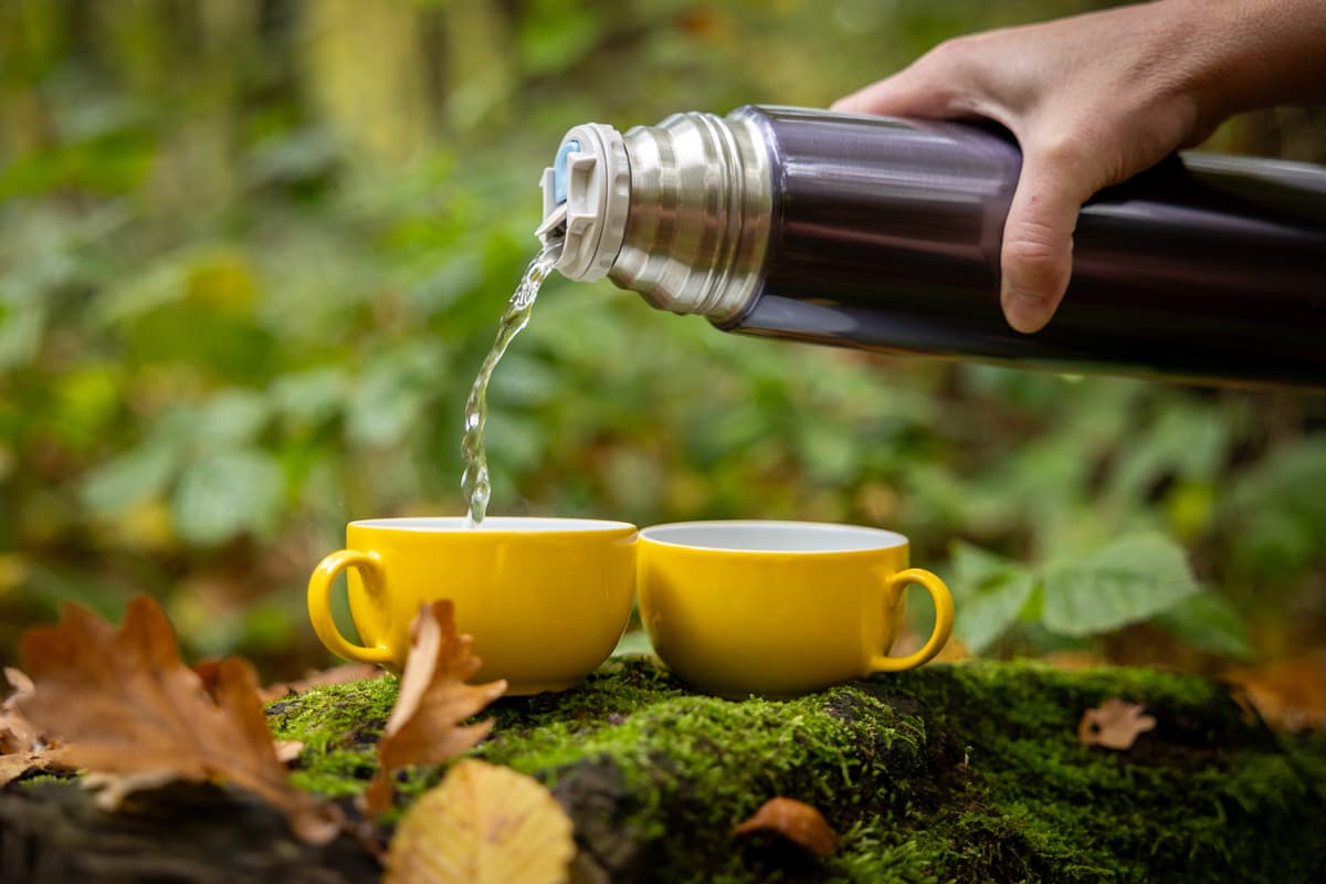 Koffie wordt uit een thermoskan in twee gele kopjes op het mos geschonken